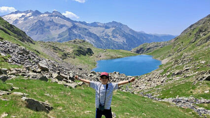 Joyful little kid portrait with Gorgutes lake and snowy Pyrenees mountains on background on a sunny summer day, Benasque, Spain.