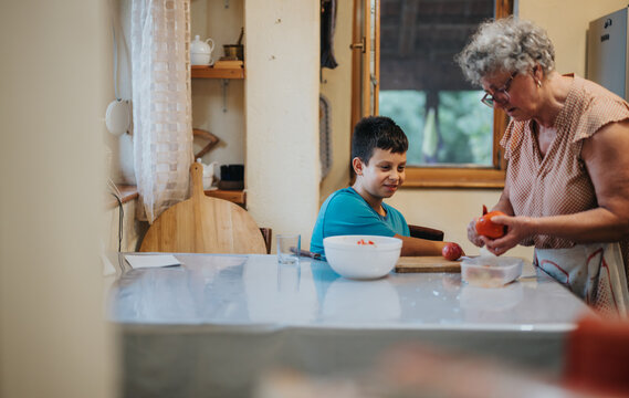 A grandmother and her grandson are enjoying quality time cooking in a warm, inviting kitchen atmosphere. The scene captures inter generational bonding and shared culinary activities.