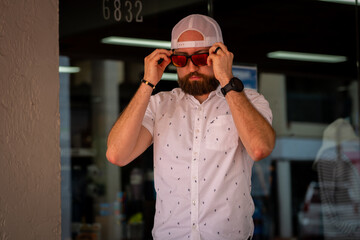 portrait of man wearing a hat adjusting his sunglasses, under shade.