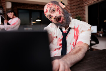 Fatigued man typing on laptop in office, looking like undead zombie, working to death metaphor....
