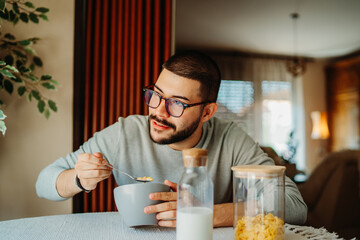 Young caucasian man eating corn flakes for breakfast at home