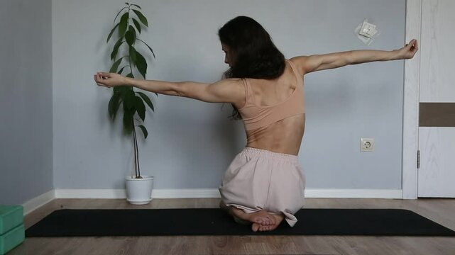 Beautiful fit atletic body woman doing stratching exersices for shoulders, scapula and healthy back in bra and sporty wear sitting on black mat at home interior. Health yoga and sport lifestyle