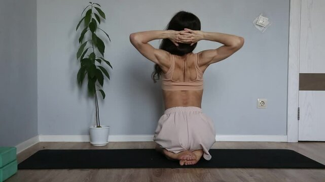 Beautiful fit atletic body woman doing stratching exersices for shoulders, scapula and healthy back in bra and sporty wear sitting on black mat at home interior. Health yoga and sport lifestyle