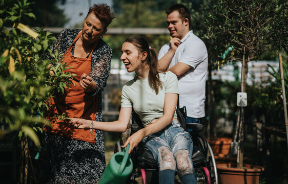 An elderly woman, a girl in a wheelchair, and a boy with Down syndrome enjoy gardening together, showcasing inclusivity and connection across generations in a sunny garden.