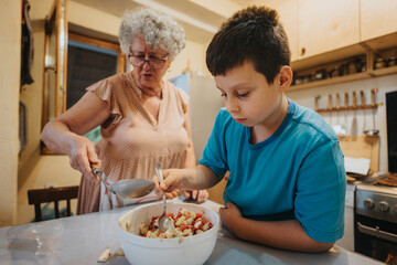 A grandmother and her grandson are seen working together in the kitchen, preparing a meal. The image captures a loving family interaction and the tradition of cooking.