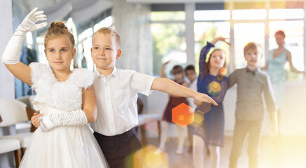 Joyful schoolboys and schoolgirls of primary classes training valse dance in events salon