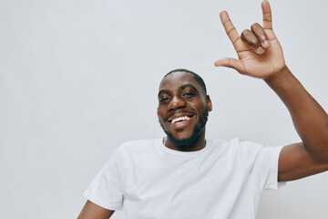 Smiling young man making a hand gesture in a casual white t shirt against a light grey background,...