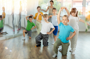 Joyous little boy and girl training waltz poses together with other attendees of dancing courses