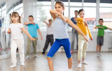 Positive juvenile girl engaged in hip-hop dance together with children's group and female trainer...