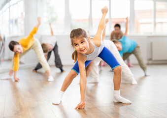 Active preteen girl practicing sport dances with other children and instructor during dancing...