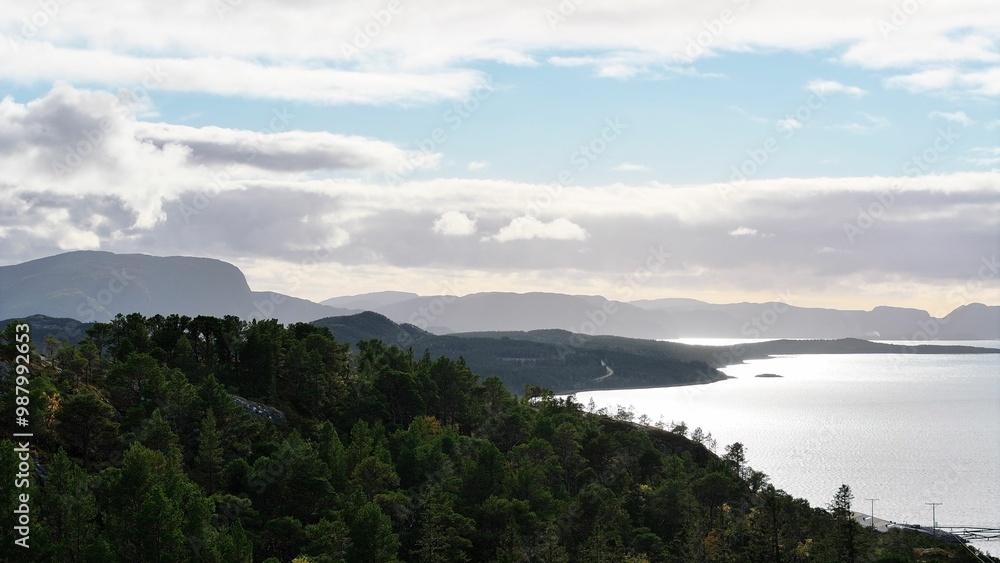 Sticker Scenic view of forest, lake, and mountains under a partly cloudy sky.