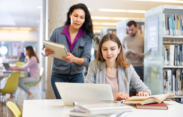 Obraz premium Young woman working with laptop and books, finding information at library
