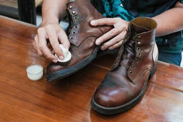 Close up of a hands polishing a leather boots with mink oil with sponge, on wooden table, shoes shining and cleaning.