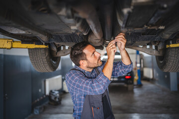 Car mechanic use a wrench to repair automobile undercarriage system