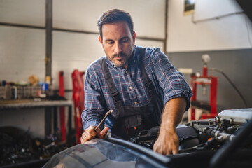 Focused car mechanic work on car engine in automotive workshop