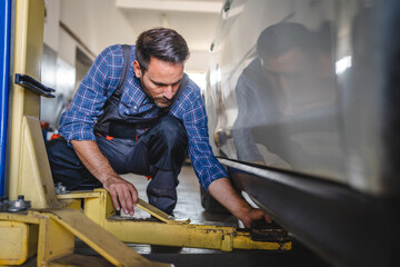 Car mechanic adjusting hydraulic lift beneath car for maintenance work
