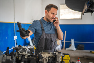 Mechanic work while on mobile phone call in auto repair workshop