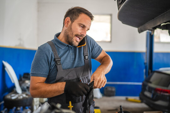 Car mechanic work on engine while talk on mobile phone in garage