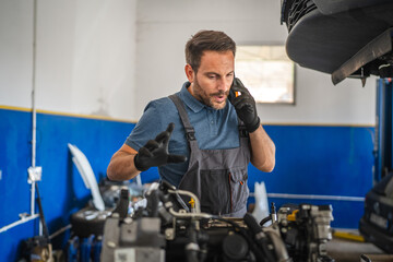 Car mechanic work on engine while talk on mobile phone in garage