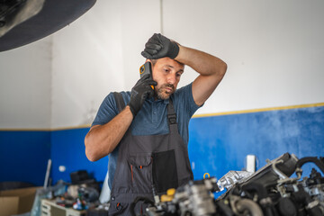 Car mechanic talk on mobile phone look stress in a workshop