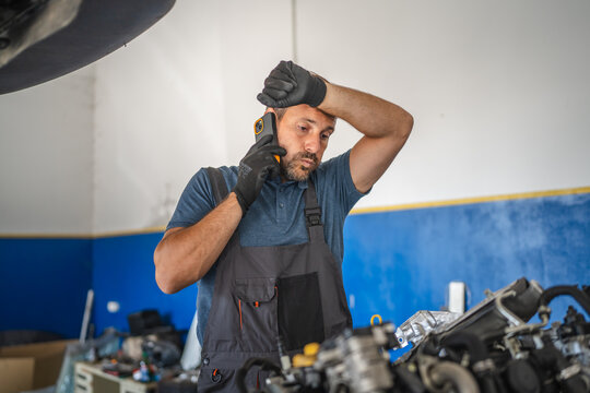 Car mechanic talk on mobile phone look stress in a workshop - Powered by Adobe