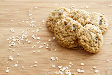 Freshly baked homemade oatmeal raisin cookies on a wooden cutting board.  Ingredients sprinkled around cookies