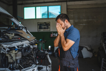 Car mechanic in a workshop look stress beside an open car hood