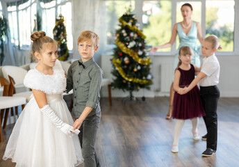 Joyful minor schoolboys and schoolgirls training valse dance in events salon adorned with Xmas tree