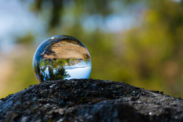 An image of a glass photographic lens ball reflecting an inverted image of a rocky shoreline.