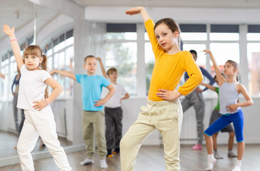 Obraz premium During dance workshop, girl with team of young like-minded children learn to dance modern dances, doing movement with unrecognizable teacher. Studio school for amateur and professional dancers