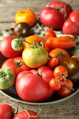 Different ripe tomatoes in bowl on wooden table, closeup
