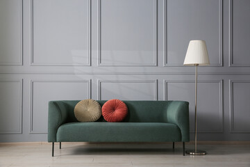 Comfortable sofa and lamp near grey wall in room