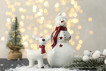 Funny snowman figure and decorative reindeer on table against blurred lights