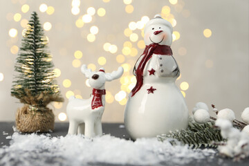 Obraz premium Funny snowman figure, decorative reindeer and artificial snow on table against blurred lights
