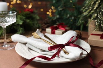 Christmas place setting with plate, napkin, cutlery and festive decor on brown table, closeup