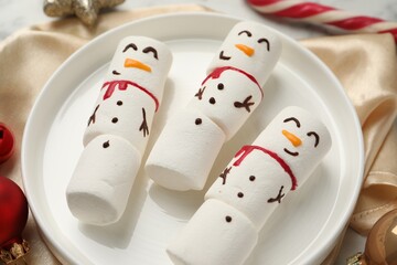 Funny marshmallow snowmen and festive decor on table, closeup