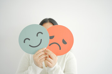 Woman hands holding sad face hiding behind happy face, bipolar and depression, mental health, split personality, mood change concept
