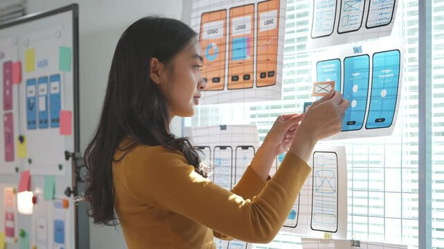 Young asian woman working as ux or ui designer is arranging pieces of paper representing wireframe prototypes of a mobile application