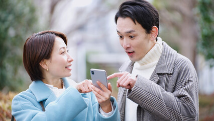 スマホを見る夫婦（冬服・コート・上着）