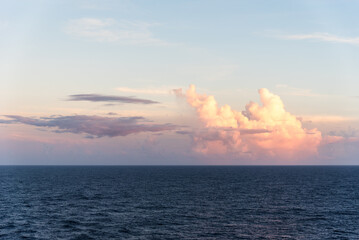 The evening sky over the tranquil Atlantic Ocean is softly illuminated by the setting sun. Light reflects off the clouds near the horizon, casting a serene glow.