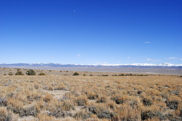 Snow-covered mountains rising up in the distance over vast high mountain desert landscape on a sunny winter day