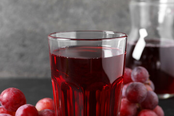 Tasty grape juice in glass and berries on table, closeup