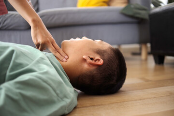 Man Doing CPR First Aid, Checking Pulse to Asian Guy at Home First Aid Emergency Rescue Concept
