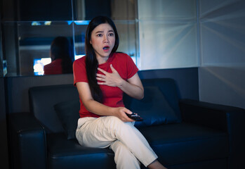 shocked and scared woman is watching horror movie TV on sofa at night