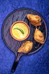 Homemade Samosa, a crispy and spicy Indian triangle shape tea time snack. Served with mustard sauce or kasundi on ablack ceramic platter. Selective focus