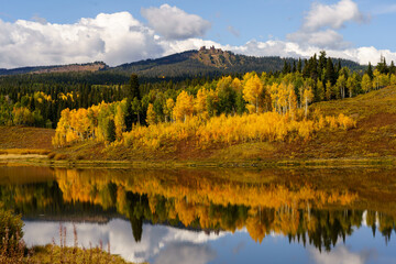 Yellow aspen trees with reflection in a lake and Rabbit ears rock formation in the background,...