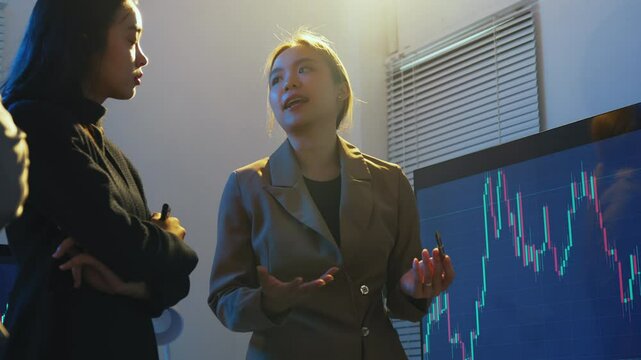 Businesswoman is giving a presentation about the stock market to her colleagues, using a large screen to show charts and graphs