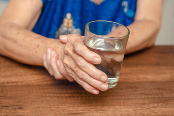 Elderly woman's hands holding glass of water, symbolizing hydration and health.