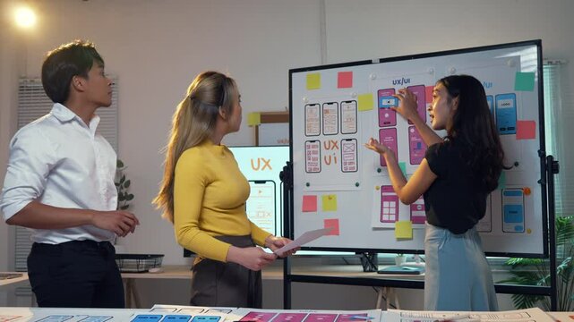 Group of asian user experience designers collaborating in an office, discussing and developing a mobile app design while utilizing whiteboards and sticky notes for brainstorming