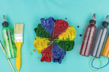 Vibrant Tie-Dye Shirt with Paint Bottles and Brush on Aqua Background